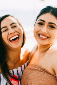 Two young woman laughing and smiling with bright white smiles from cosmetic dental care in Lafayette, CO